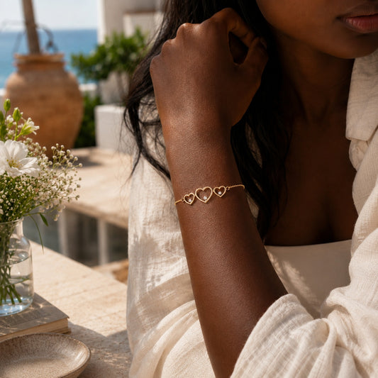 Goldmasons triple hearts gold bracelet worn on the wrist in a luxury Mediterranean resort setting.