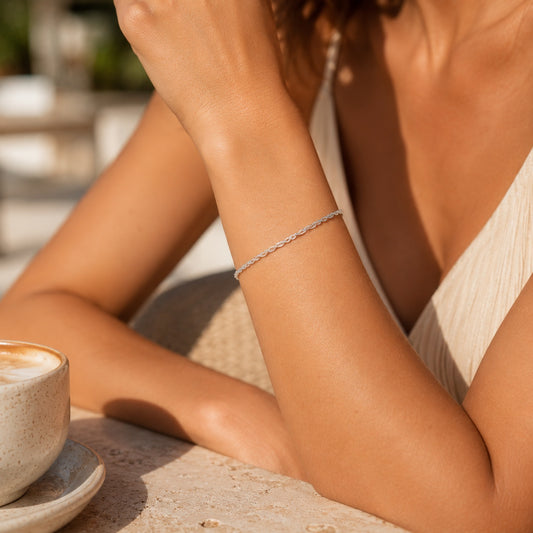 Goldmasons 925 sterling silver Singapore chain bracelet worn on the wrist in a luxury outdoor café setting.