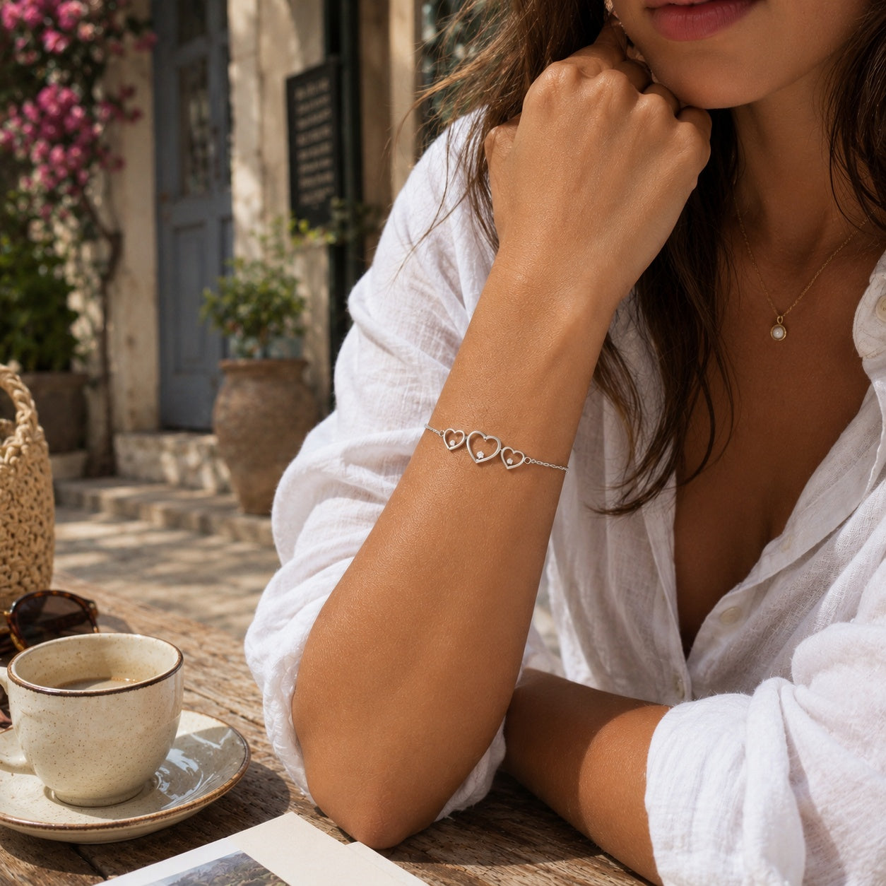 Goldmasons triple hearts sterling silver bracelet worn on the wrist in a sunlit Mediterranean café terrace setting.