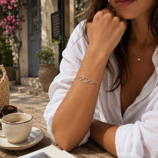 Goldmasons triple hearts sterling silver bracelet worn on the wrist in a sunlit Mediterranean café terrace setting.